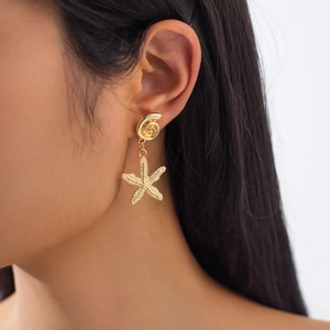 Macro detail of gold sea snail stud and textured starfish drop earring on model