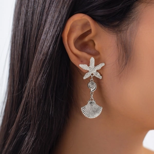 Detail of silver starfish and seashell drop earrings worn by a model in close-up