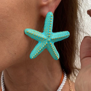 Primer plano de un pendiente de estrella de mar azul con textura dorada de estilo playero