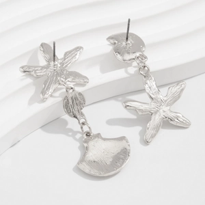 Detailed view of silver starfish and seashell drop earrings on a white wavy background
