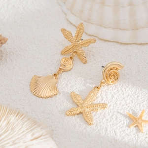 Close-up of golden beach theme earrings with starfish and seashell charms on white sand