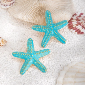 Detalle de un colgante de estrella de mar azul cielo sobre arena blanca con conchas marinas
