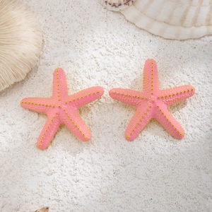 Primer plano de colgantes de estrella de mar rosa con puntos dorados sobre arena de playa