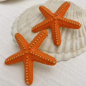 Detalle de pendientes de estrella de mar naranja vibrante con puntos dorados sobre concha
