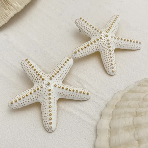 Detalle de pendientes de estrella de mar blanco cálido con textura dorada sobre arena