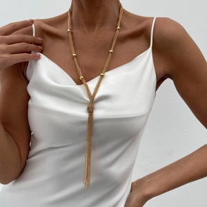Detail of layered gold chain necklace with metallic beads and elegant knotted tassel
