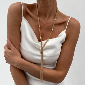 Fashionable long gold tassel chain necklace with CCB beads worn on a white silk dress