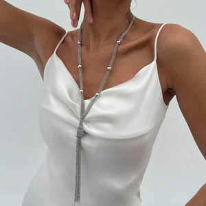 Detail of silver long tassel Y-necklace with metallic beads on elegant white satin