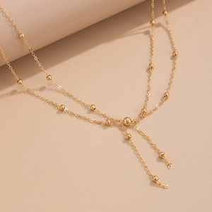 Detail of a layered golden body chain featuring polished beads and Y-shaped tassel pendant
