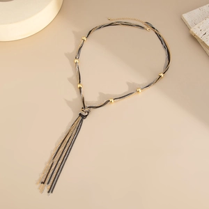 Detail of multi-color woven metal tassel necklace with gold beads on beige background