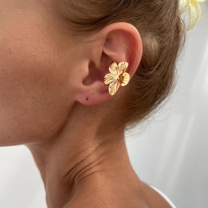 Detailopname van een gouden bloem oormanchet met getextureerde bloembladen op een model