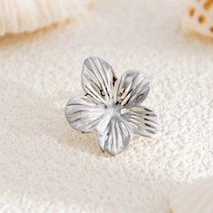 Detailed close-up of a silver flower earring with textured petals on a sandy background