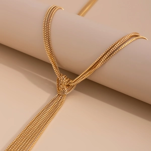 Detail of layered gold tassel necklace with decorative knot on minimalist metal chains