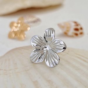 Macro shot of silver five-petal flower earring with radial texture on a seashell