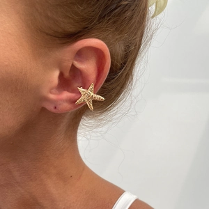 Detail of a golden starfish ear cuff featuring spiral textures and engraved dot patterns