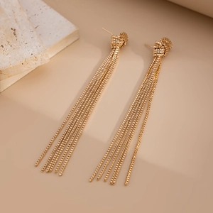Detail of long gold tassel earrings with woven metal ball and polished box chain texture