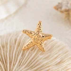 Macro view of gold starfish earring with hammered texture on white coral background