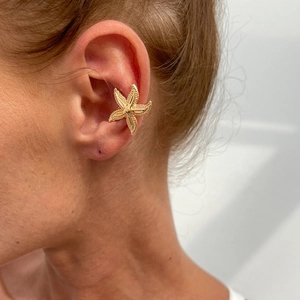 Detailed close-up of golden starfish-shaped cuff earring on ear with textured metallic finish
