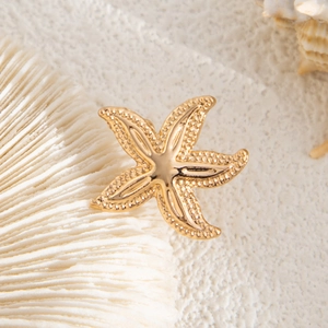 Detailed close-up of a golden starfish earring set with textured finish on coral