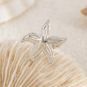 Detailed view of starfish brooch with embossed texture on sand and coral background