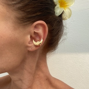 Detail of golden crescent moon ear cuff with facial relief on a model with plumeria