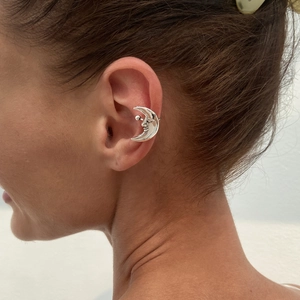 Detailed view of a silver crescent moon ear cuff featuring an artistic facial engraving