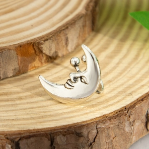 Macro view of a polished silver crescent moon ear cuff with a smiling face carving