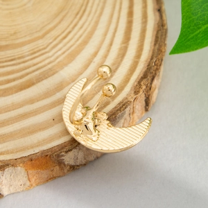 Detail of a textured golden crescent moon earring with small spheres on a wooden tray