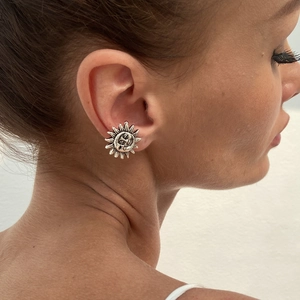 Detailed view of silver sun stud earrings with face relief worn by a model