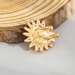 Macro detail of golden sun-shaped alloy ear cuff on a natural wood surface background