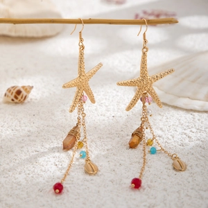 Detail von Strand-Seestern-Ohrringen mit bunten Perlen und Quasten auf sandigem Holzzweig