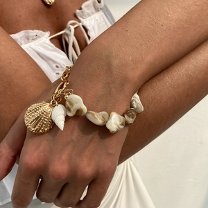 Detail eines Muschelarmbands mit goldenen Gliedern am Handgelenk für den Strand