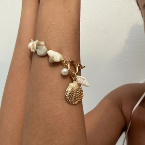 Detailansicht des Muschelarmbands im Meeresstil mit Goldkette und weißen Perlen am Handgelenk