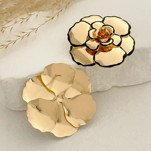 Detailansicht goldener Blumenohrringe mit schwarzem Rand auf weißem Marmoruntergrund
