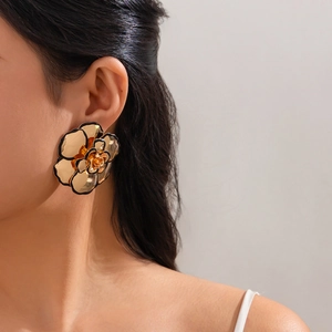 Nahaufnahme eines großen goldenen Metall-Blumenohrrings mit schwarzen Kanten am Model