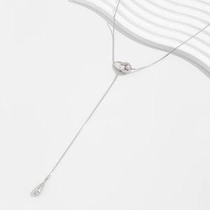 Macro detail of silver snake chain with metallic heart slide and teardrop pendant