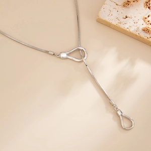Detail of silver snake chain necklace featuring elegant horseshoe clasps on beige surface