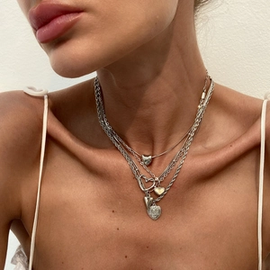 Détail de colliers superposés argentés avec pendentifs cœur et chaînes torsadées