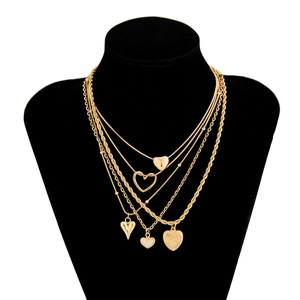 Détail de colliers dorés superposés avec pendentifs coeur gravés sur un buste noir