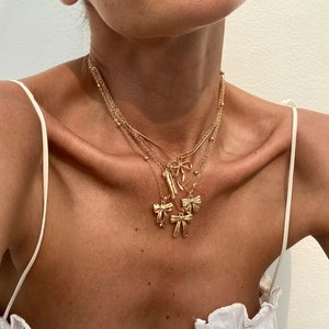 Détail de colliers dorés superposés avec nœuds et pendentifs cœurs portés par un mannequin