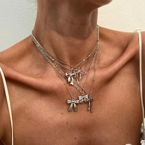 Détail de colliers superposés argentés avec pendentifs nœuds portés par un modèle