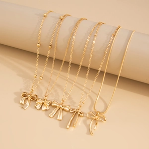 Détail de cinq colliers dorés superposés avec divers pendentifs nœuds sur un présentoir