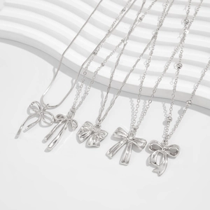 Détail de pendentifs nœuds argentés sur diverses chaînes avec un fond blanc épuré