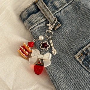 Détail d'un bijou de sac gâteau fraise avec nœud et perles accroché à un jean bleu