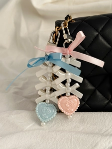 Detail of balletcore style heart and bow pearl charms on a black quilted bag