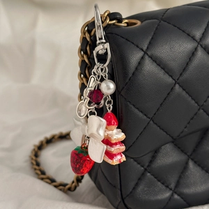 Détail du pendentif gâteau fraise avec nœud perlé sur une lanière de sac noir