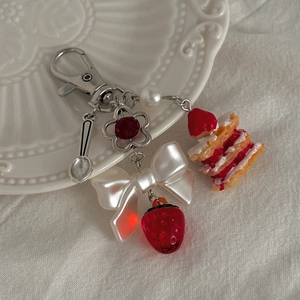 Détail d'un porte-clés gâteau à la fraise avec nœud posé sur une assiette en porcelaine