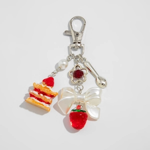 Détail d'un porte-clés gâteau aux fraises avec nœud et perles sur fond blanc immaculé
