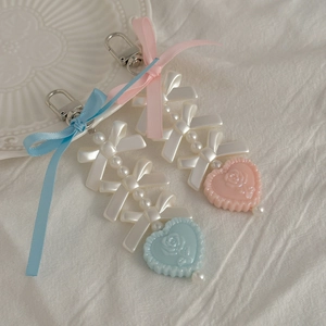 Pink and blue pearl bow heart keychain with rose engraving on a soft white cloth background