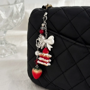 Porte-clés pendentif fraise et gâteau avec nœud blanc sur un sac matelassé